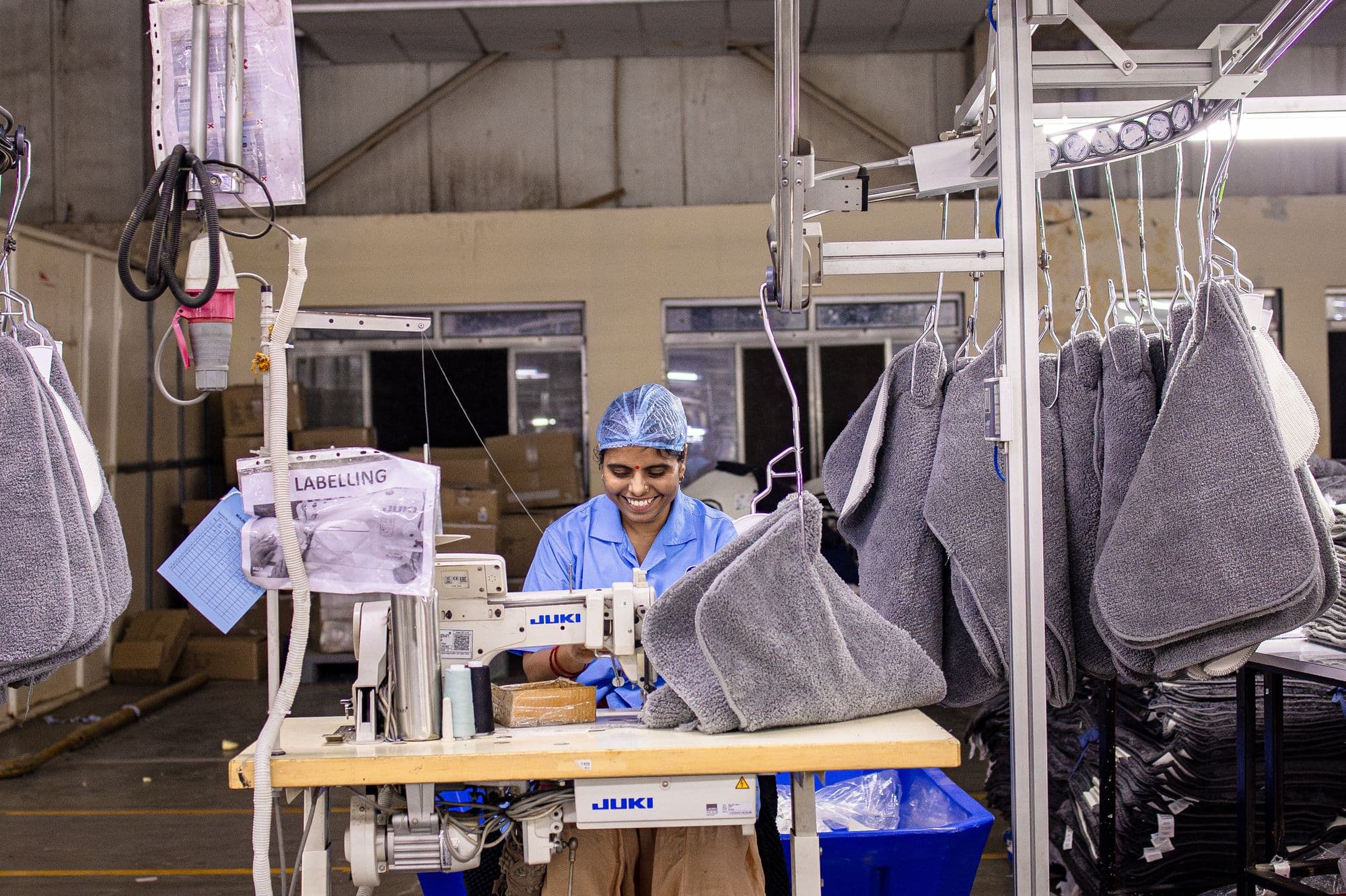 A tailor sewing samples beside rows of hanging garments